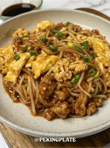A delicious-looking bowl of easy stir-fried minced beef with enoki mushrooms and scrambled eggs. The dish is coated in a savory brown sauce and garnished with freshly chopped green onions, with a small bowl of soy sauce in the background.